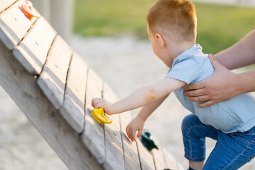 A cute happy caucasian toddler boy of three or four years old climbs a artificial climbing rock...
