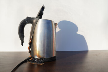 Burning Electric kettle. Electric kettle for tea caught on fire over table. Electric kettle melted due to a short circuit in electrical wiring. Overloaded electrical current or short in device