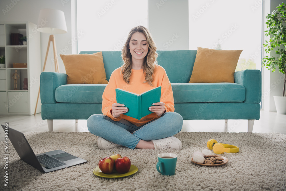 Poster Full body photo of nice young girl sit floor read book netbook snacks studying wear orange clothes modern interior flat indoors