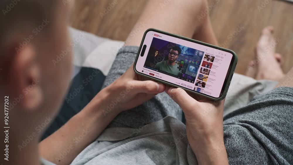 Poster close up of caucasian teen boy watching video about color grading on mobile phone while sitting on s
