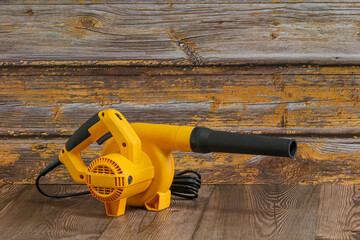 Yellow electric handheld air blower. It has a long nozzle to be a powerful tool, likely used for cleaning or clearing debris with wooden surfaces.