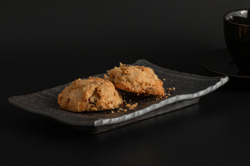 Delicious cookies contain dried fruits or berries like cranberries or raisins, giving them a rustic, homemade look on a ceramic plate against a black background and a teacup.