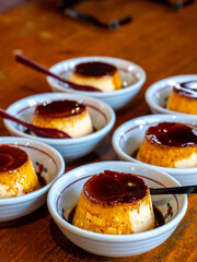 A delightful array of egg puddings served in small ceramic bowls. The golden, creamy desserts are topped with a rich layer of caramelized sugar, with spoons ready for a delicious, sweet treat