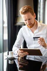 Successful handsome business man holding credit card, using digital tablet. Online shopping concept