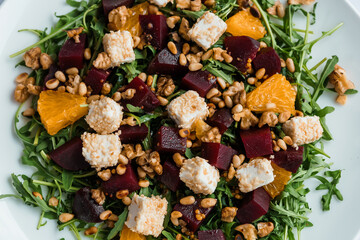 Vegetable salad with arugula, cheese, orange and beets on a white plate