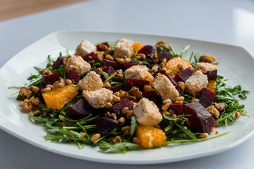 Vegetable salad with arugula, cheese, orange and beets on a white plate