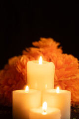 Vertical image showing three candles burning brightly, surrounded by marigold flowers