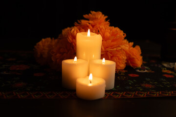 Three candles emit a warm light, surrounded by marigold blooms.