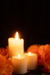 Vertical image of three candles flickering on the left, surrounded by marigolds in shades of orange