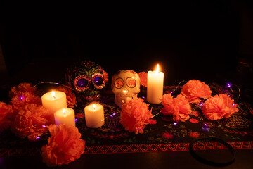 A vibrant Day of the Dead altar with two skulls: one adorned with metallic flowers, the other...