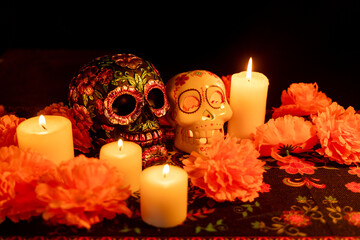 Two skulls on a black background: one adorned with metallic flowers and the other hollow with a lit candle inside