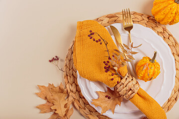 Autumn table setting with pumpkin decorations on light background. Empty plate, cutlery, yellow...