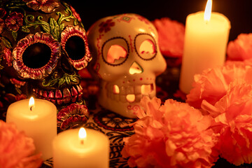Close-up of two skulls on a Día de los Muertos tablecloth. One skull is decorated with metallic flowers, while the other contains a lit candle