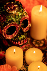 Vertical image showing a skull with metallic floral decorations, surrounded by orange calendulas and lit candles