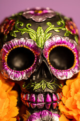 Detailed close-up of a skull decorated with metallic flowers and surrounded by lively orange blooms