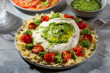 Farfalle pasta with burrata cheese, cherry tomatoes and green pesto on gray background.