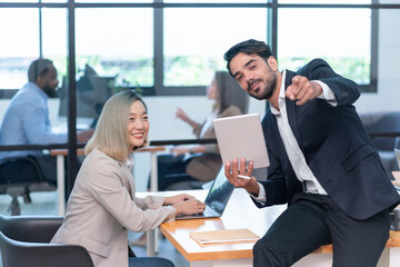 multiracial business people working in the office room,businessman sitting on desk holding tablet and pointing something,businesswoman typing laptop and smile,they are talking during break