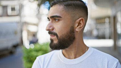 A handsome man with a beard stands thoughtfully on a city street, embodying urban masculinity and...