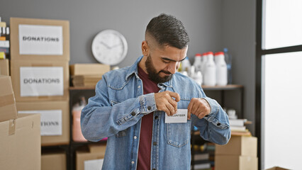 A young man attaches a volunteer badge in a storehouse filled with donation boxes.
