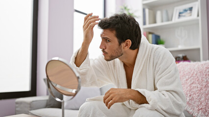 A young hispanic man in a robe grooming in a well-lit home interior.