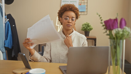 African american woman working from home, reviewing documents in front of a laptop in a cozy living room. - Powered by Adobe