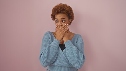 A surprised african american woman with hands over mouth against a pink background