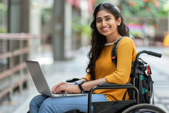 A young smiling female student with disability sitting in wheelchair using a laptop 