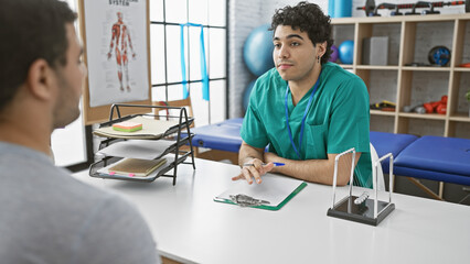 Obraz premium In a well-equipped physiotherapy clinic, a male therapist consults with a patient, symbolizing healthcare and rehabilitation indoors.