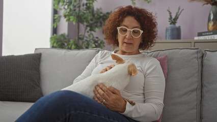 An elderly woman sits in a living room while holding and petting a small chihuahua on a couch, capturing a serene indoor moment of companionship with her pet.