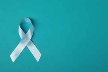 Light blue ribbon on teal background, top view with space for text. Prostate cancer awareness