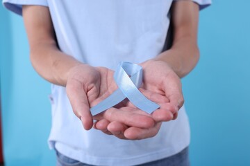 Prostate cancer awareness. Man holding light blue ribbon as symbol of support on color background,...