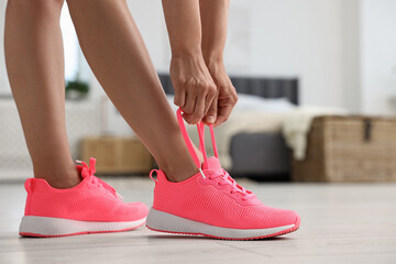 Naklejka premium Woman tying shoelace of pink sneaker indoors, closeup. Space for text