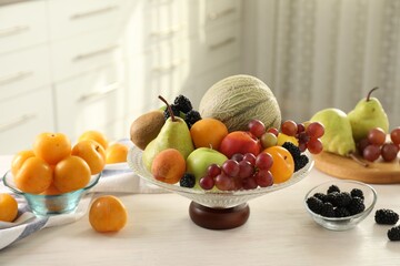 Glass vase with different fruits and berries on white table indoors