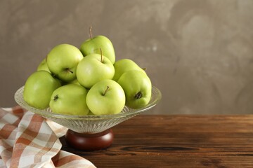 Glass vase with fresh green apples on wooden table against gray background, space for text