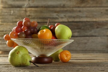 Glass vase with different fresh fruits on wooden table, space for text