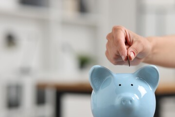 Woman putting coin into piggy bank against blurred background, closeup. Space for text