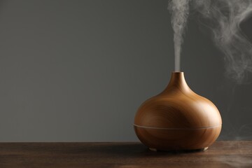 Aroma oil diffuser with steam on wooden table, space for text