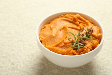Delicious mashed sweet potatoes with walnuts and rosemary in bowl on light table, closeup. Space for text