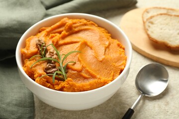 Delicious mashed sweet potatoes with walnuts, rosemary, spoon and bread on light table, closeup