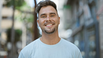 A handsome young hispanic man with a beard smiles joyfully on an urban street.