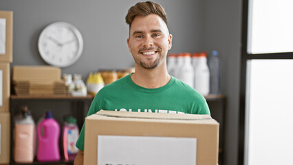 Handsome hispanic man smiling while holding a box in a cluttered warehouse setting.