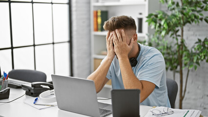 A stressed young man with headphones at his modern office workspace