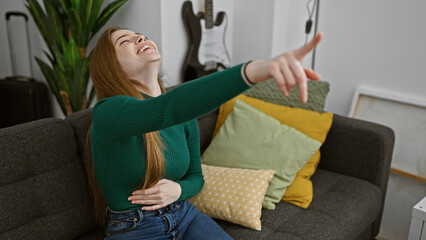 A cheerful young woman with long blonde hair enjoying a moment alone in her cozy living room, filled with cushions and a sofa.