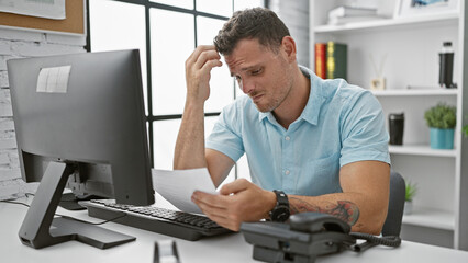 Fototapeta premium Hispanic man with beard in light blue shirt feeling stressed at modern office workplace while reading documents