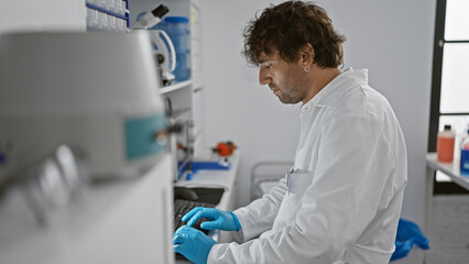 A focused man with a beard works meticulously in a bright laboratory setting, typing on a computer.