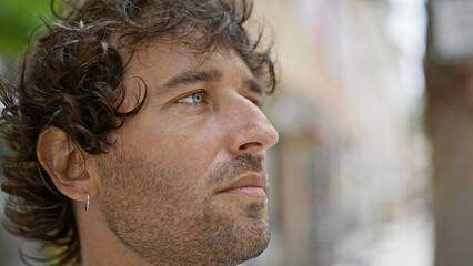 Obraz premium A contemplative young hispanic man outdoors in an urban street setting, looking away from the camera.