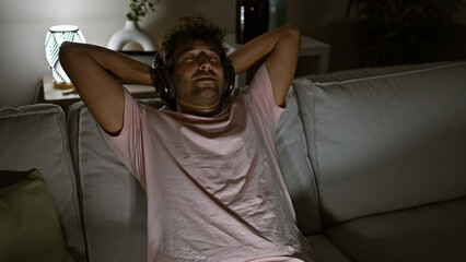 Relaxed hispanic man enjoying music with headphones in a cozy living room at night