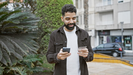 Fototapeta premium Handsome young adult hispanic man with beard holding credit card and smartphone on city street.