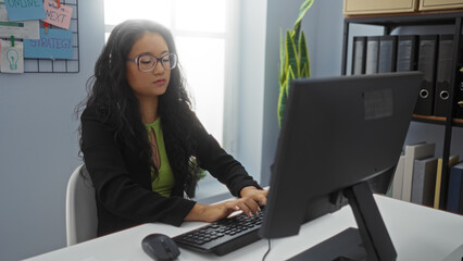 Woman working in an office on a computer with files and notes on the wall
