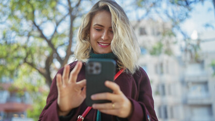 A young blonde woman smiling while using a smartphone in a sunny outdoor park setting